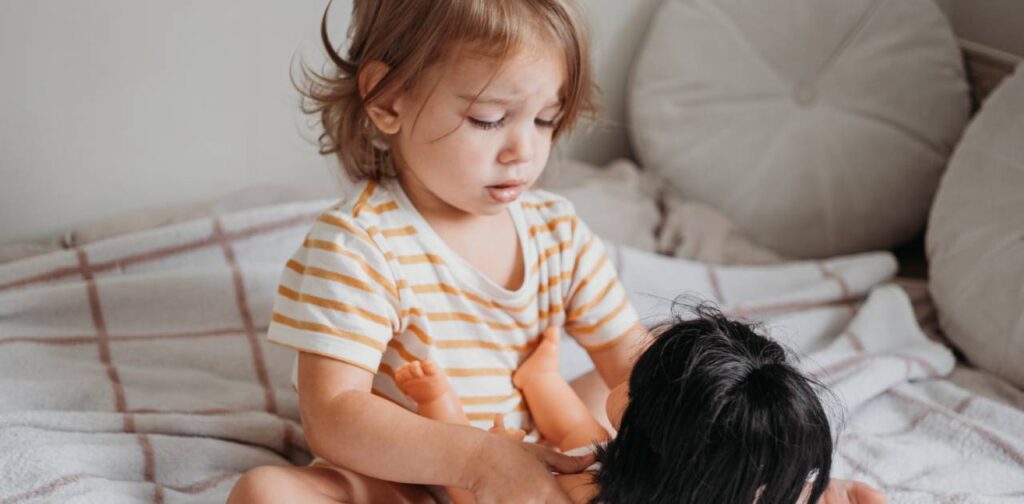 enfant et sa poupée dans un lit parapluie poupon